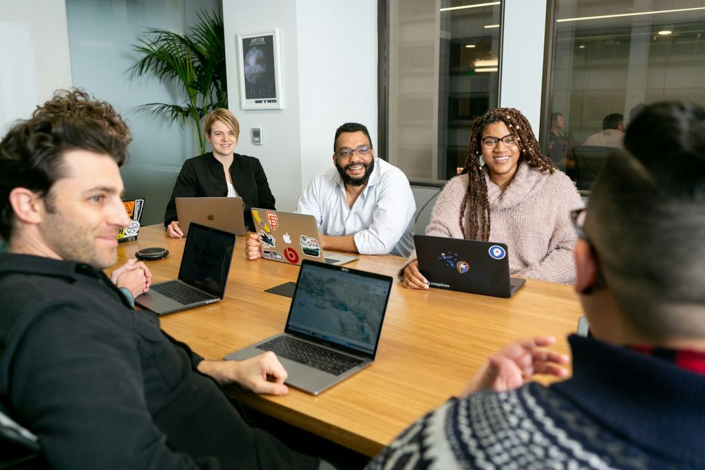 Photo by Mapbox four people all on laptops, two men and two women, listen to person talking in a board meeting